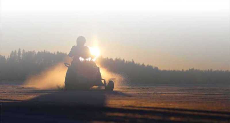 Snowmobiler riding at sunset